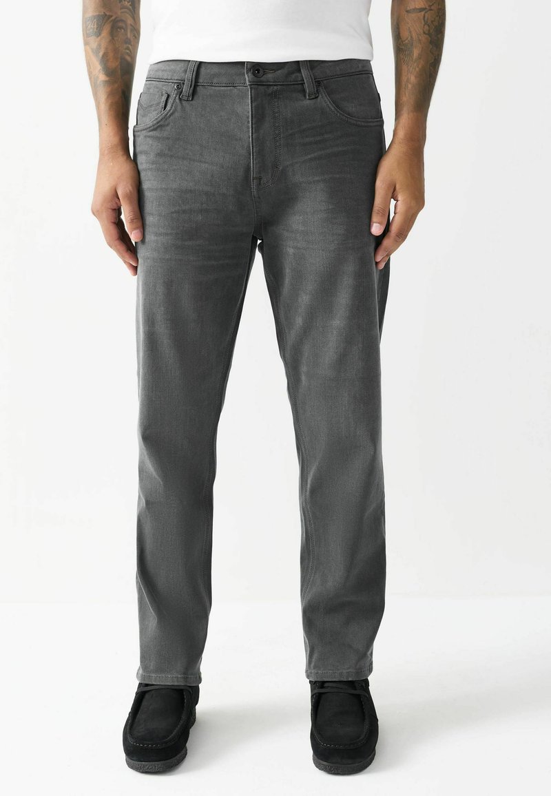 Grå denim jeans med slim fit, fem-lommer design og knaplukning. Bæret med sorte ruskind sko, der viser en glat tekstur.