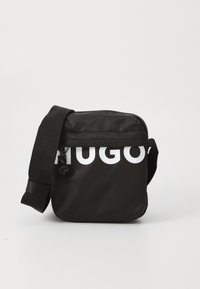 Bolso negro de bandolera con una superficie texturizada, que presenta un logo blanco. Incluye una correa ajustable y cierre con cremallera. Forma cuadrada compacta.
