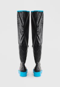 Black, glossy knee-high boots with a textured back panel and blue rubber sole. Features a contrasting blue trim at the top and zippers.