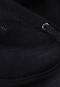 Black fabric featuring a smooth texture with a sewn edge, metal grommet, and black cord threaded through for fastening.
