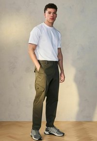 Hvid kortærmet t-shirt parret med olivenfarvede cargo-bukser med sidelommer, suppleret med grå atletiske sneakers.