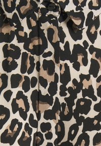 Koszula z guzikami w serek w wzór lamparta, w odcieniach brązu i czerni, o gładkiej teksturze i z wyłamiancem w kształcie stożka.