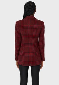 Rot karierter Blazer mit schwarzen Akzenten, taillierte Passform, Reverskragen und langen Ärmeln. Aus strukturiertem Stoff gefertigt, mit einem klassischen Karomuster.