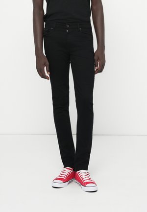 Black slim-fit jeans with front pockets, a zipper fly, and a single button closure, paired with red low-top sneakers.