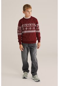 Burgundi kötött pulóver fehér geometrikus mintákkal és pöttyökkel, fehér ing fölött viselve, sötétszürke farmernadrággal és szürke sportcipőkkel párosítva.