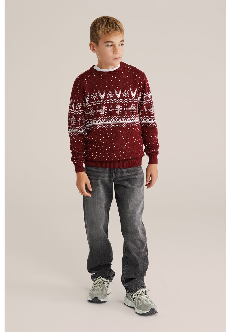 Burgundi kötött pulóver fehér geometrikus mintákkal és pöttyökkel, fehér ing fölött viselve, sötétszürke farmernadrággal és szürke sportcipőkkel párosítva.