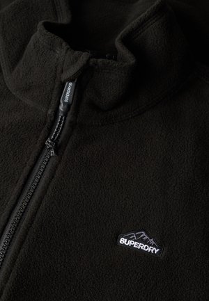 Black fleece jacket featuring a half-zip closure, high collar, and a small embroidered logo on the left side. Soft texture and lightweight design.