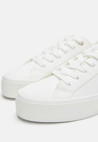 Fehér bőr sportcipők texturált felsőrésszel, kerek orral és lapos gumitalppal. Fehér fűzőkkel és finom varrási részletekkel rendelkeznek.