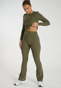 Olivgrön träningsjacka med långa ärmar och utsvängda leggings i elastiskt tyg, med en sömlös design och subtila sömnadsdetaljer.