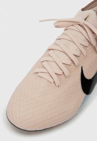 Ροζ πλεκτό αθλητικό παπούτσι με αντίστοιχους κορδόνες και μαύρο λογότυπο Nike στο πλάι, με φόντο λευκό.