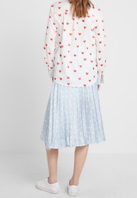 Vit skjorta med röd hjärtapplikation, kombinerad med en ljusblå veckad kjol med vitt stjärnmönster, samt vita sneakers.