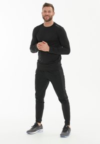 Sort langærmet skjorte og sorte atletiske bukser lavet af letvægtsstof. Sættet har et tætsiddende design og kontrastdetaljer.
