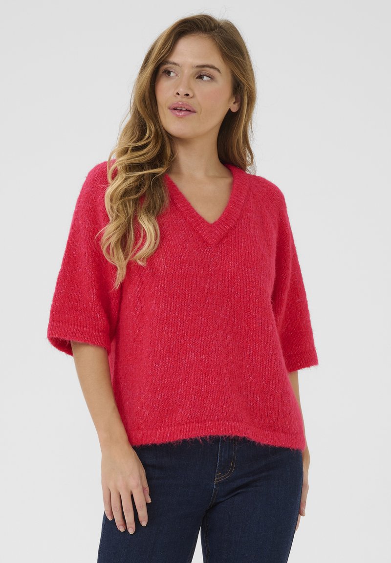 Pull ras du cou à manches courtes, en V, de couleur rose vif, fabriqué dans un tissu texturé doux avec une coupe décontractée. Ourlet légèrement effiloché en bas.