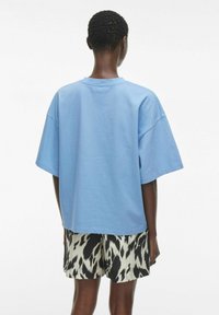 Lyseblå bomulls oversized t-skjorte med rund hals, korte ermer og avslappet passform, kombinert med shorts med svart-hvitt mønster.