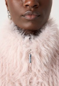 Fluffy roze kraag met een gestructureerd oppervlak en zilveren hardware-details. Het kledingstuk heeft een rits met branding bij de nek.