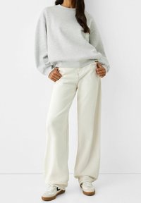 Gray sweatshirt with a relaxed fit, paired with cream wide-leg pants. Footwear features a white base with brown soles and black accents.