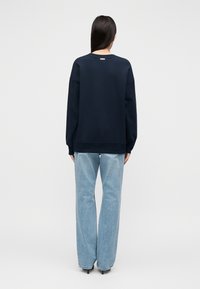 Φαρδιά μπλε σκούρα φούτερ με στρογγυλή λαιμόκοψη, μακριά μανίκια και ελαστικές μανσέτες. Συνδυασμένο με ανοιχτό μπλε καμπάνες τζιν.