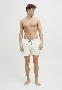 Costumi da bagno da uomo in beige chiaro, con vita elastica e cordino nero, tasche laterali e piccolo logo sulla gamba sinistra.