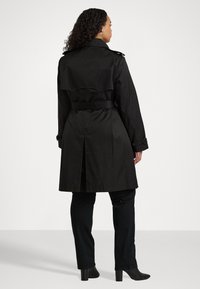 Svart trench coat med axelklaffar, bälte i midjan och en slits bak. Slätt tyg med en klassisk design.