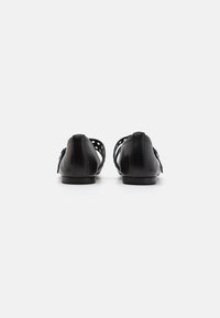 Chaussures noires en cuir avec un talon bas, présentant un design découpé et une texture lisse. Bout arrondi et accents minimalistes.