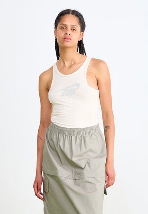 Beige ribbed tank top with a light grey Nike logo, paired with a light grey elastic-waist skirt featuring side pockets.