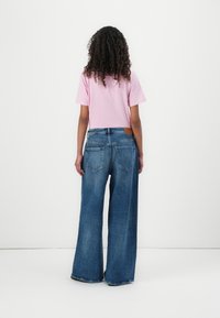 Tricou roz cu mânecă scurtă, asortat cu blugi denim cu picioare largi, având un design clasic cu cinci buzunare și o etichetă din piele la talie.