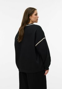 Czarna bluza o luźnym fasonie, z okrągłym dekoltem i kontrastowym jasnym obszyciem wzdłuż szwów na ramionach. Miękka w dotyku.