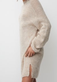 Sukienka sweterkowa w jasnobeżowym kolorze, o luźnym kroju, z okrągłym dekoltem, długimi rękawami oraz bocznymi rozcięciami zapewniającymi swobodę ruchów.
