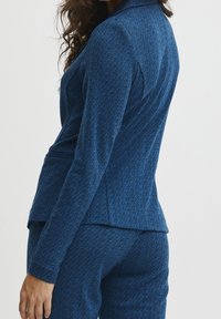 Modrý sako s rybím vzorem, přiléhavého střihu, dlouhými rukávy a hladkou texturou, spárované s kalhotami ve stejném designu.