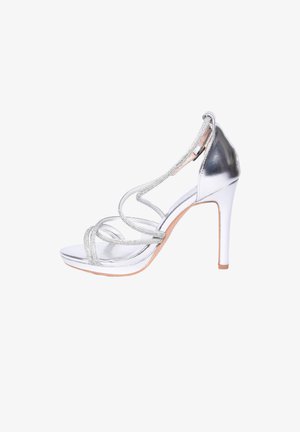 Sandalo argentato con tacco alto, cinturini incrociati impreziositi da strass e chiusura con fibbia alla caviglia, punta aperta e tacco stiletto sottile.