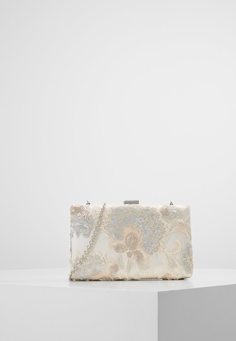 Pochette rectangulaire blanche avec paillettes argentées, broderies florales et une bandoulière chaîne argentée, posée sur un socle blanc sur fond uni.