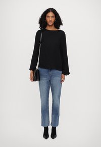 Μαύρη υφασμάτινη μπλούζα με μακριά μανίκια, μπλε τζιν παντελόνι με ίσια γραμμή, μαύρες ankle boots με τακούνι και μια μικρή μαύρη τσάντα με αλυσίδα.