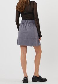 Jupe grise texturée avec une taille élastique, tombant au-dessus du genou. Associée à un haut noir transparent et des mocassins épais noirs.