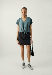 Jasnoniebieska, krótka koszula z guzikami, wiązana w talii, w zestawie z czarną dżinsową spódnicą mini i szarymi tenisówkami. Czarna torba na ramię.