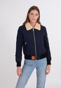 Marine bomberjack met een beige nep-shearling kraag, geribbelde manchetten, een ritssluiting aan de voorkant en een oranje label op de zoom. Gladde stoftextuur.