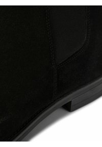 Bottine en daim noir avec panneau latéral élastique et talon bas superposé sur fond blanc.