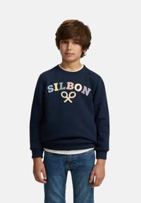 Sudadera azul marino con bordado de "SILBON" en colores pasteles. Puños y cuello acanalados, combinada con una camiseta blanca debajo y jeans de mezclilla.