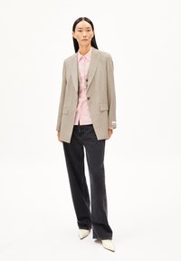 Beige checkered blazer with notch lapels, paired with a light pink shirt and dark jeans. Stiletto heels complete the outfit.