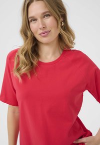T-shirt rossa con una texture a costine, scollatura rotonda e maniche corte. Presenta una vestibilità rilassata e un tessuto morbido su uno sfondo neutro.