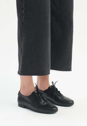 Scarpe in pelle nera con punta rotonda, chiusura con lacci e tacco basso. Indossate con pantaloni in denim neri a vita alta, tagliati e sfilacciati.