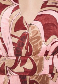 Robe multicolore avec un profond décolleté en V. Le tissu a une texture brillante avec des motifs abstraits en nuances de rose, marron et crème.