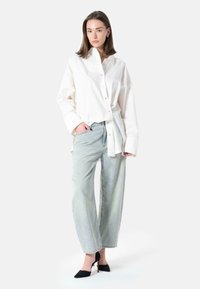Hvit oversized skjorte med knapp og lomme, kombinert med lyseblå vide jeans og svarte spisse hæler. Enkelt og strukturert design.