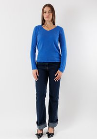 Maglione azzurro a maniche lunghe con scollatura a V realizzato con un tessuto morbido. Abbinato a jeans scuri, leggermente risvoltati alle caviglie, e scarpe nere con punta affusolata.