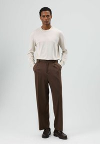 Lichtbeige shirt met lange mouwen gecombineerd met bruine, op maat gemaakte broek. Het shirt heeft een ronde hals, de broek heeft een rechte pasvorm en voorzakken.