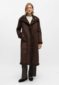 Manteau en shearling marron avec un col oversized texturé, doté de fermetures à boutons, de poches à rabat et de détails de coutures contrastés.