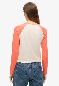 Langermige raglan t-shirt met perzikkleurige mouwen en een crèmekleurig lijfje. Zacht katoenen materiaal, ronde halslijn, en een casual pasvorm, gecombineerd met denim jeans.