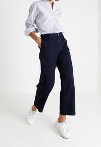 Dark blue wide-leg denim trousers with a high waist, paired with a light blue button-up shirt and white sneakers.