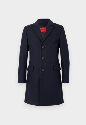 Manteau en mélange de laine marine avec un col cranté, cinq boutons, deux poches avant et une coupe structurée. Texture lisse et design sur mesure.