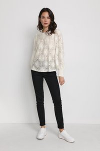 White lace top with floral patterns, long sleeves, and smocked wrist cuffs, paired with black slim pants and white sneakers.