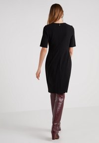 Svart figurnära klänning med korta ärmar och dragkedja i ryggen, kombinerad med knälånga burgundy läderstövlar med klack.